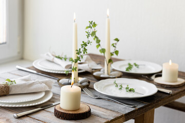 Rustic zero waste wedding decor with natural elements. Wooden table, candles, linen napkins, branches with green leaves. Eco-friendly decoration for the special dinner. Romantic and cozy place
