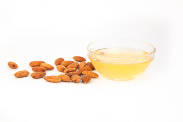 Sweet almond oil in glass bowl, first extraction, and dry almond nuts as ingredient for confectionery close up on white backgrounds