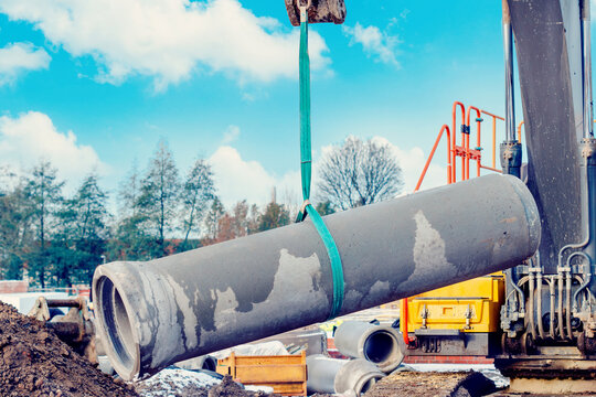 Concrete drainage pipe lifted by excavator during deep drainage works on construction site