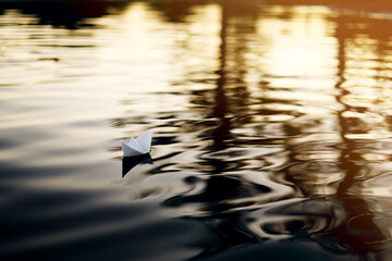 A paper boat is floating on the waves in the water at a beautiful sunset. Origami ship Sailing. The...