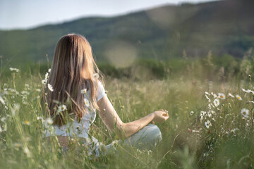 Beautiful young woman with long blonde hair meditates in nature, in a beautiful field. Travel and...