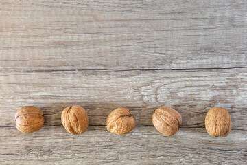 Brown wooden texture background and row of five whole walnuts copy space