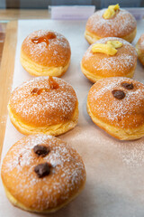 Different flavour donuts, sprinkled with powdered sugar, displayed in a bakery