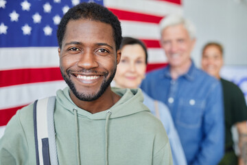 Head and shoulders portrait of smiling black man in line with diverse group of people voting...