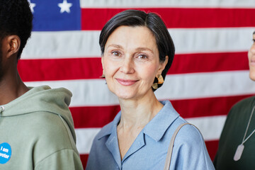 Head and shoulders portrait of smiling mature woman in row with diverse group of people voting...
