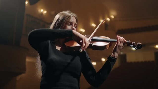 young woman musician is playing violin in music hall, portrait of woman with fiddle