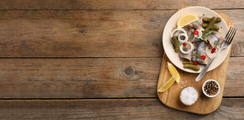 Salted herring fillets served with thyme, pickles, onion rings, chili pepper and lemon on wooden table, top view with space for text. Banner design