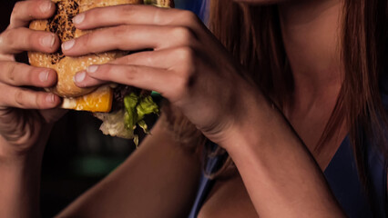 Young beautiful starving girl makes a big bite on a juicy fresh meat burger