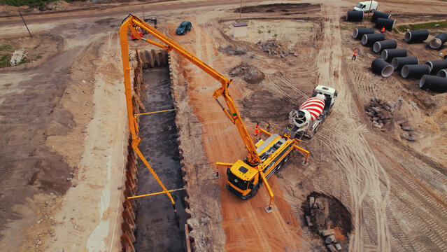 Heavy big machinery during road works. A yellow crane filling up a long hole with fresh cement. High quality photo