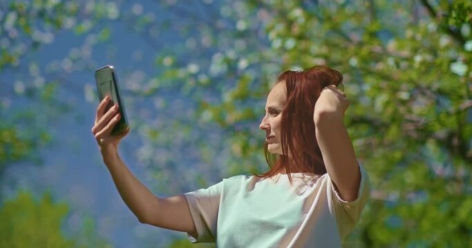 adult woman is taking selfie by smartphone in blooming garden in spring day, 4K, Prores