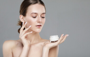 Beautiful cute pretty charming woman is holding a cream jar isolated on grey color background