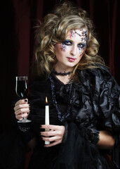 Young beautiful woman in a witch costume with bright makeup and hairdo is holding a candle. Halloween.