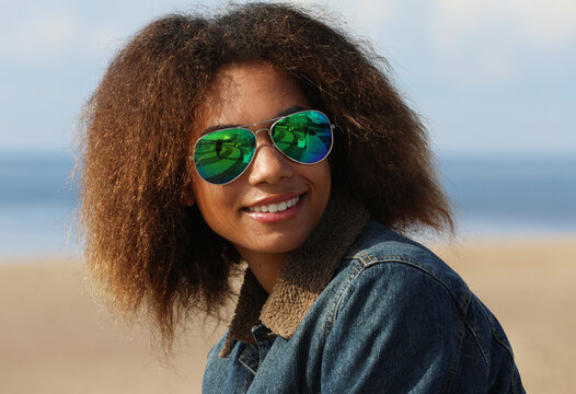 Beautiful young african woman in a denim jacket and sunglasses on the beach on a summer day.