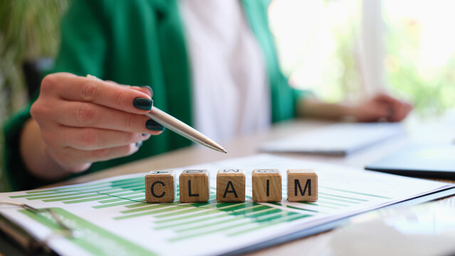 Woman pointing with pen on word claim made with wooden cubes in row