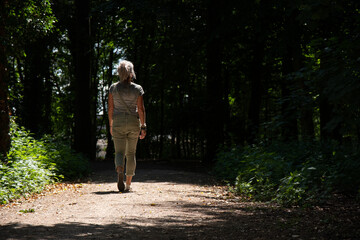 A caucasian woman with blond hair walking on a path in the sunlight in an otherwise dark forest