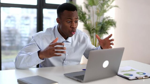 Irritated shocked african american male, office worker, product manager, annoyed yelling at a laptop during online video conference with colleagues, sit in a modern office, frustrated by result work
