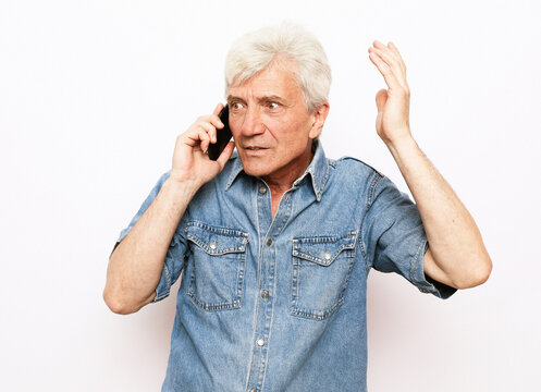 An elderly man dressed in denim shirt holds a smartphone and hears good news.
