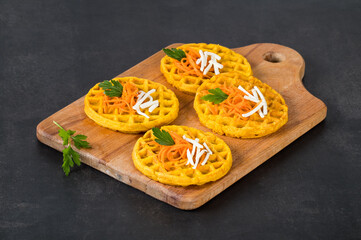 Round carrot waffles on a wooden board. Dark gray background