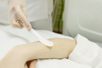 Close-up of the cosmetologist's hand using a spatula, we apply the gel for epilation on the client's hand. Laser hair removal procedure.
