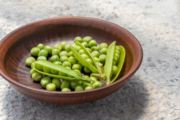 Green peas in ceramic bowl. On stone countertop. Pisum sativum - L. Open pods and peeled sugar peas. Rustic style