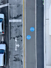 A picture from above from a road with a pre-sorting area with two cars in it, a second empty pre-sorting area with two arrows, a bike path with two blue circles with a bike in it and a walkway