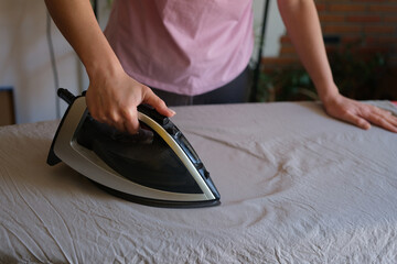 Housewife ironing wrinkled bedsheet on board using steam iron