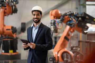 Automation engineer uses tablet for programming robotic arm in factory.