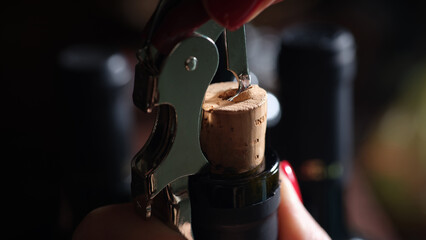 Female hands with red manicure opening bottle of wine using corkscrew
