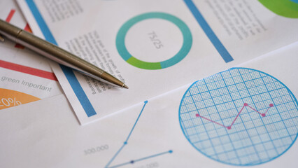 Metal pen on documents with colourful charts, graphs and diagrams