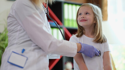 Female pediatrician examining little child with stethoscope.