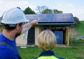 Man and woman solar installers engineers with tablet while installing solar panel system on house,...