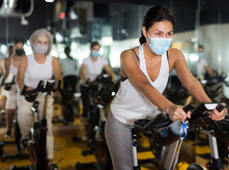 Portrait of young adult woman wearing face mask for disease protection training on stationary bike workout in gym