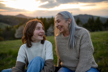 Happy senior grandmother with teenage granddaguhter sitting on grass, talking and having nice time...