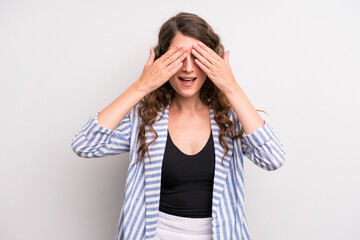 young adult pretty woman smiling and feeling happy, covering eyes with both hands and waiting for...