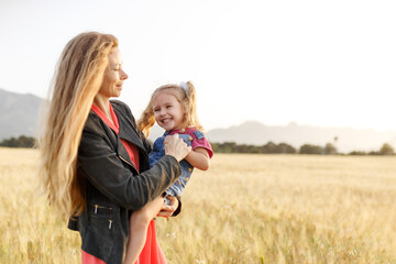 Portrait of a happy young mother and her lovely daughter playing and laughing in a field of wheat . Freedom concept.