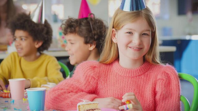 Portrait of girl sitting at table with party blower celebrating birthday with  piece of birthday cake - shot in slow motion