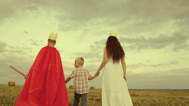 happy family. boy son with mother plays red cape superhero meadow. happy family concept. chidhood dream. golden crown on his head. child dream kid protect help group people. teamwork. fantastic game.