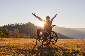 Woman sitting on a wheelchair enjoying sundown on mountain background.