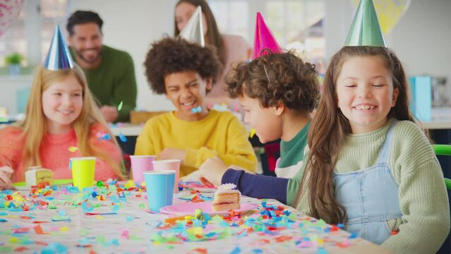 Portrait of girl sitting at table for party celebrating birthday blowing colourful confetti towards camera - shot in slow motion