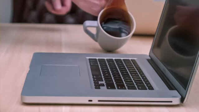Cup of coffee spilling on a laptop keyboard in slow motion; 4k 1000fps