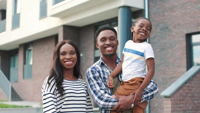 Close up of African American joyful cute family parents with small kid boy looking at camera and smiling while standing on street. Little son with happy mom and dad outdoor Love, parenthood, childhood