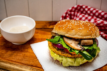 Vegan veggie protein burger, with tomato, arugula, red onion, mushrooms and avocado mayonnaise on a wooden board and a white background. Chopped view. Copy text.