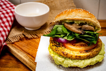 Vegan veggie protein burger, with tomato, arugula, red onion, mushrooms and avocado mayonnaise on a wooden board and a white background. Chopped view. Copy text.