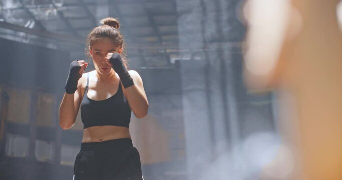 Cinematic shot of Professional female boxer practising shadow boxing in cross training workout space. Young asian woman fighter exercising in abandoned building dark hall gym. working out on her moves