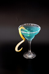 Curacao, a cocktail with ice, lemon zest and sugar around the edge of a glass on a black background.