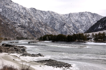 A clearing in the frozen bed of a beautiful river surrounded by snow-capped mountains.