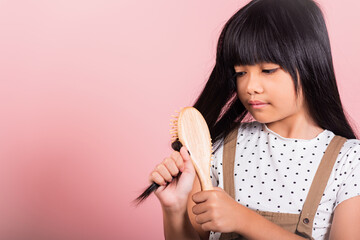 Asian little kid 10 years old hold comb brushing her unruly she touching her long black hair at studio shot isolated on pink background, Happy child girl with a hairbrush, Hair care concept