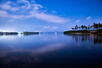 beautiful lake at night with blue and dark sky, palm trees in the background and reflections in the...