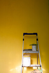 ladder with paint cans and space for text on yellow wall 
