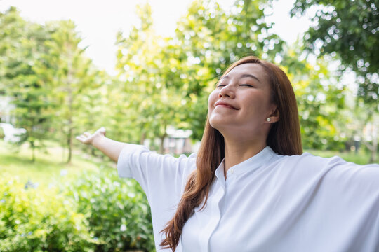 Portrait image of a young asian woman with opened arms enjoying in the park